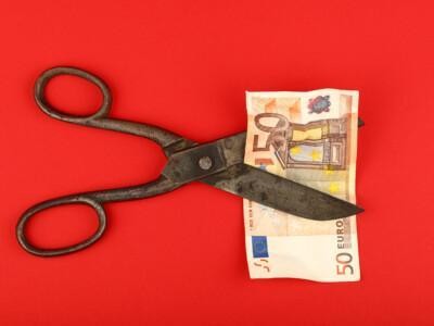 Vanhat ruostuneet sakset leikkaamassa 50 euron seteliä. Kirkkaanpunainen tausta.